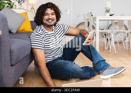 Young Indian man smiling with phone at home Stock Photo