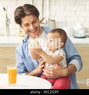 Father Enjoys Quality Time With Infant Son While Playing With a Colorful Toy in the Kitchen Stock Photo