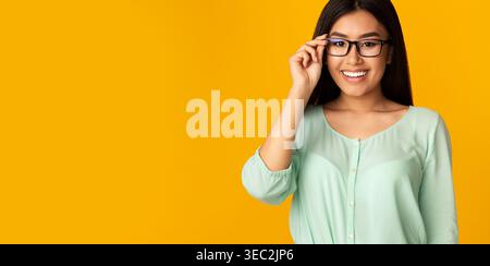 Young Woman Wearing Glasses Smiles Warmly Against a Bright Yellow Background Stock Photo