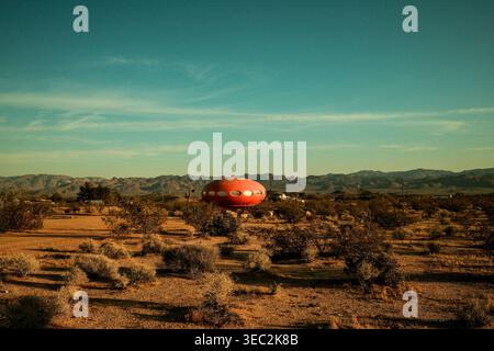Isolated red dome structure in the California desert surrounded by dry landscape and distant mountains under a bright blue sky. Stock Photo