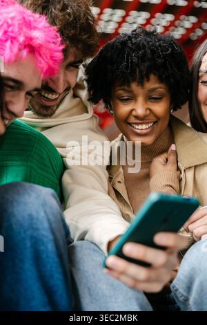 Diverse group of students sitting on campus stairs using phones together Stock Photo