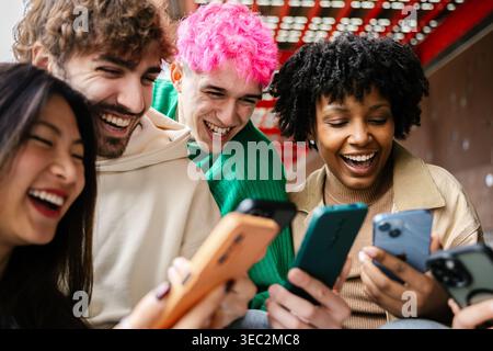 Diverse group of students sitting on campus stairs using phones together Stock Photo