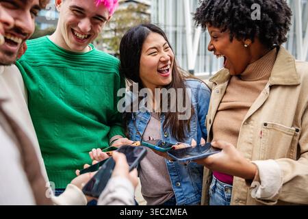 Multiracial friends using mobile phones and laughing Stock Photo