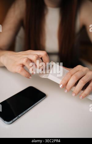 Close-up of female hands with manicured nails carefully opening white retail package containing new phone adapter cable, ready to connect and charge. Stock Photo