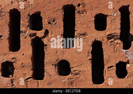 Close-up of a red clay brick showing vertical perforations and rough surface texture, highlighting masonry detail, earthy tones and industrial charact Stock Photo