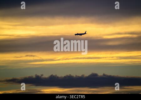A silhouette of a commercial airplane flying through a dramatic golden sunset sky above the Tamsui Bridge in New Taipei City, Taiwan. Stock Photo