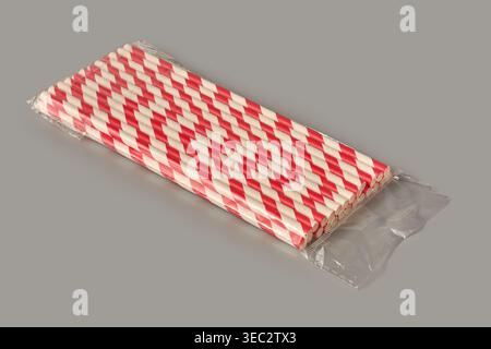 red and white striped paper drinking straws in clear plastic sleeve on grey background, eco friendly party supplies, mock-up template angle view Stock Photo