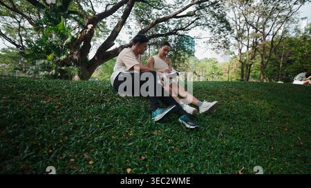 Students collaborating on homework, sitting on bench amid urban greenery and sunlight Stock Photo