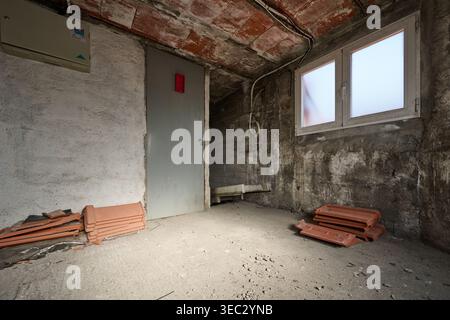 Rough concrete walls and exposed brick ceiling in an empty, unfinished room during construction or renovation featuring roof tiles Stock Photo