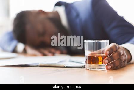 Drunk employee with glass of whiskey sleeping at working place Stock Photo