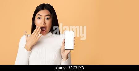 Surprised Woman Holding Smartphone With Blank Screen Against Bright Beige Background Stock Photo