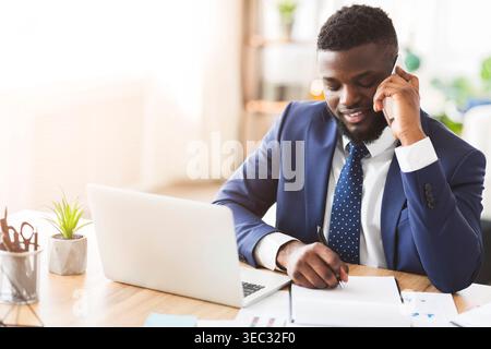 Smiling businessman talking by phone with secretary, writing down notes Stock Photo