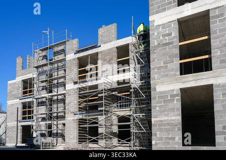 Worker on scaffolding at concrete block building under construction with open floors and blue sky Stock Photo