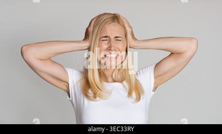 Stressed Mature Woman Covering Ears And Become Angry Stock Photo