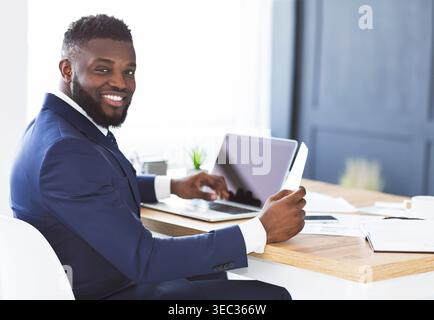 Cheerful black general manager checking reports, sitting in office Stock Photo