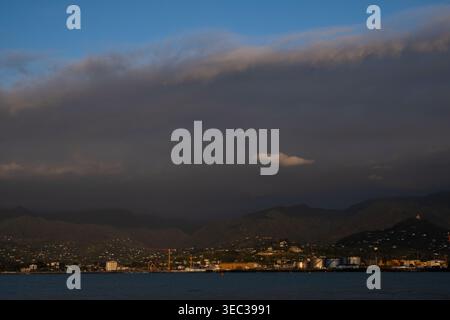 Dramatic clouds rolling over a coastal city and mountains at sunset Stock Photo
