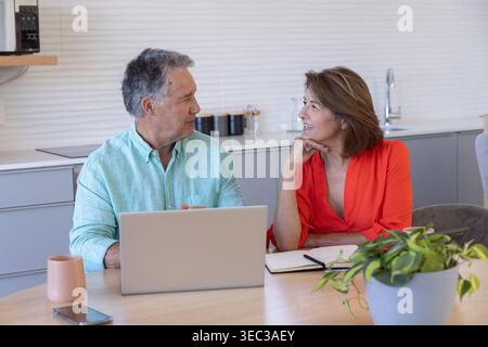 Couple with senior woman and mature man discussing bills using laptop and notebook at kitchen Stock Photo