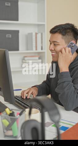 Man holding smartphone to ear with hand while typing on computer in a building; focused productivity. Stock Photo