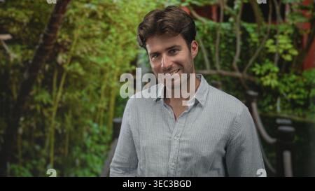 Man standing with crossed arms on a wooden bridge in a forest setting, green outdoors; pensive reflection. Stock Photo