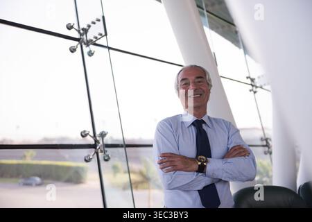 Confident Middle Eastern businessman smiling with arms crossed in modern corporate office lobby Stock Photo