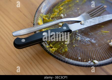 Dirty plate with fork and knife resting on wooden table after meal Stock Photo