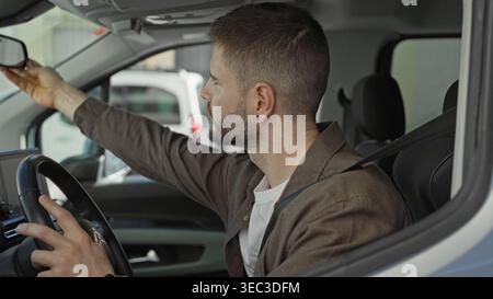 Man reaches to adjust rearview mirror with hand while wearing seatbelt in car on street; concentration. Stock Photo