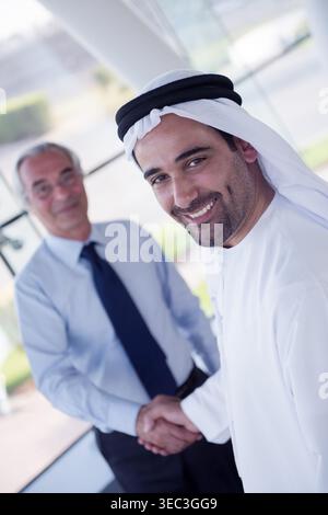 Business handshake between two businessmen in a modern office with traditional white robe and friendly smile Stock Photo