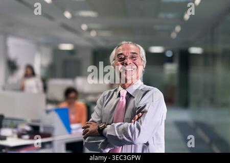 Confident senior businessman smiling in modern open plan office with colleagues and leadership presence Stock Photo