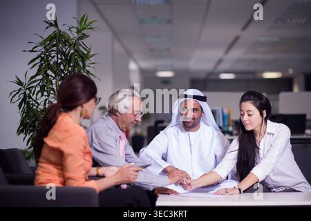 Middle Eastern business team meeting in modern open office with colleagues collaborating on documents Stock Photo