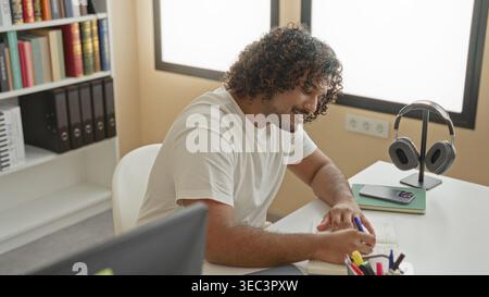 Man writing in notebook at desk in a library building, pen to lips thinking gesture; focused study and learning. Stock Photo