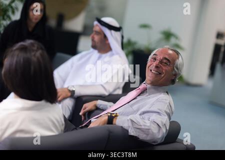 Smiling senior businessman in pink tie during relaxed corporate meeting with colleagues in modern office Stock Photo