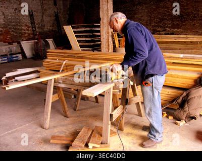 White male senior volunteer at Habitat for Humanity's Restore, cutting lumber with an electric circular saw, New Orleans, LA.  MR Stock Photo