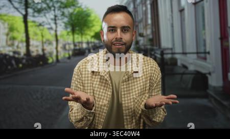 Man points finger to camera on street showing tattooed hand and beige checked shirt; community connection confidence. Stock Photo