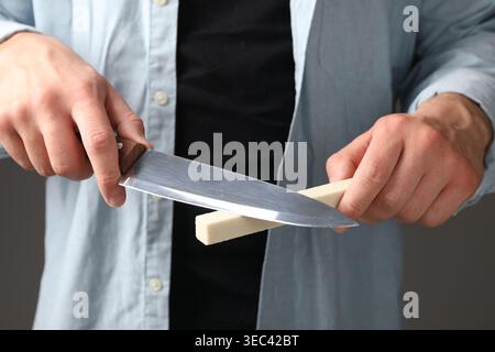 Man sharpening knife on grey background, closeup Stock Photo