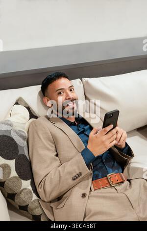 Smiling businessman in a suit lying on a sofa using his mobile phone Stock Photo
