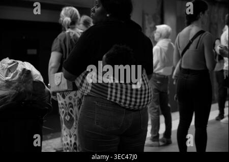 Mother carrying baby in sling at Lisbon Metro platform in black & white with commuters around Stock Photo