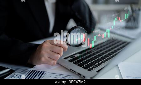 Business professional analyzing financial data trends on a laptop computer with a magnifying glass for investment insights and market research Sigmoid Stock Photo