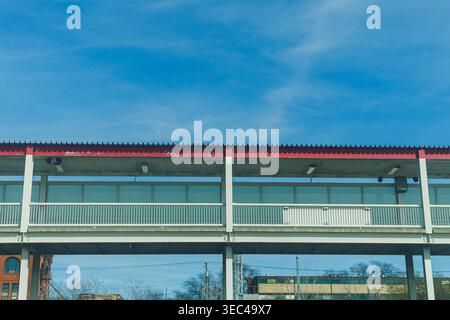 A structure rises above the ground with a simple design and narrow walkway. Sunlight shines on the overhead area. Clouds float in the blue sky, adding Stock Photo
