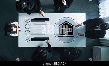 A business meeting focused on a real estate project, showcasing professionals collaborating with checklists and a house icon to refine strategies and Stock Photo