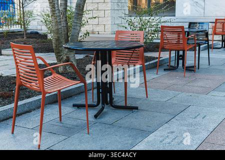 Outdoor seating area with red chairs and a black table near a building during daylight in an urban space Stock Photo