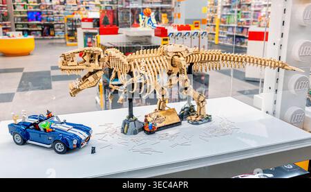 19 October 2025, Belgrade, Serbia: LEGO Tyrannosaurus Rex skeleton model displayed with a blue car in a bright modern toy store, showcasing popular br Stock Photo