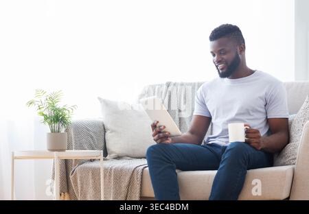 Man Enjoying Coffee While Reading on Tablet in Cozy Living Room Stock Photo