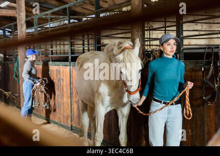 Portrait of young woman with a white horse in stable Stock Photo