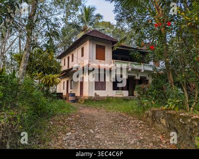 Traditional two storey village house in Kerala, India, with weathered walls and tiled roof in a tropical rubber plantation setting Stock Photo