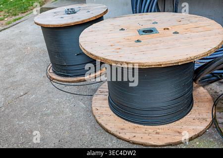 Large wooden cable spools wound with black electrical wire on site, ready for installation in construction and utility projects Stock Photo