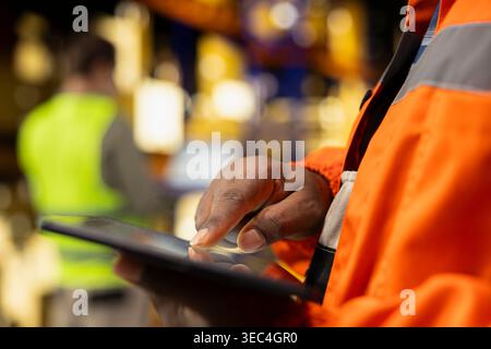 Close up of black staff managing cardboard boxes logistics on tablet in industrial storage facility, manual labor combined with package tracking ensures safe shipping dispatch, organization. Stock Photo