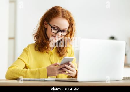 Freelance woman using smartphone near laptop computer in office Stock Photo
