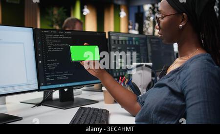 Green screen phone used by woman in company workplace doing tech quality assurance. Woman in office watches tutorial on programming languages with chroma key smartphone Stock Photo