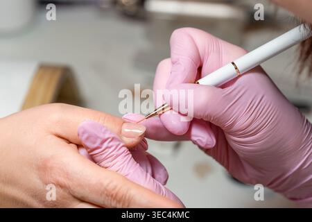 Professional nail technician wearing pink gloves performing delicate nail art design on a client's fingernail in a beauty salon Stock Photo