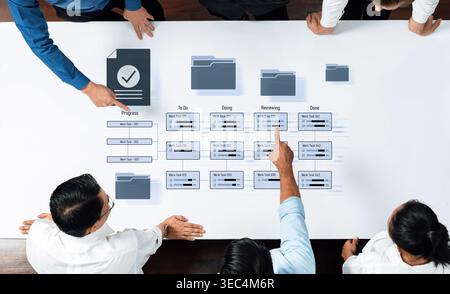 A top-down view of a collaborative workspace where team members engage in project management discussions, utilizing digital tools and organized Stock Photo